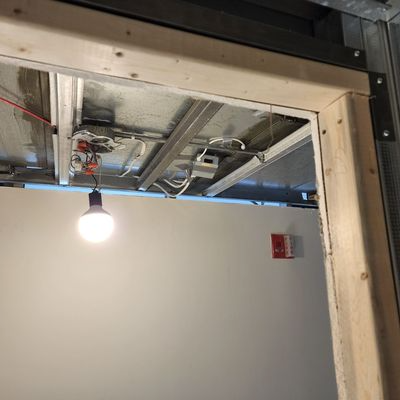 Bare ceiling with exposed beams and a lit hanging bulb above a white wall with a red sign