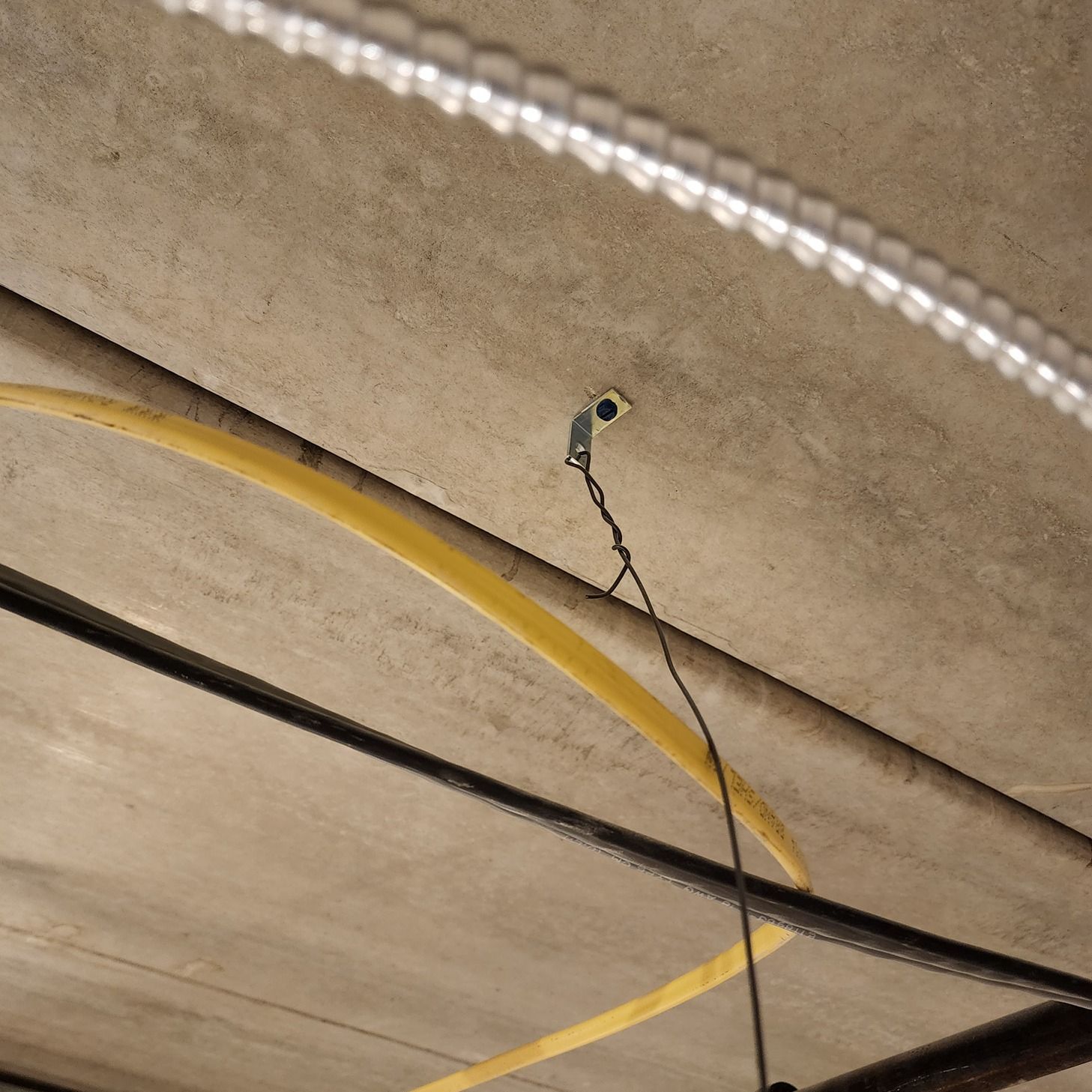 Cables hanging from a concrete ceiling, with a yellow cable looped across the frame