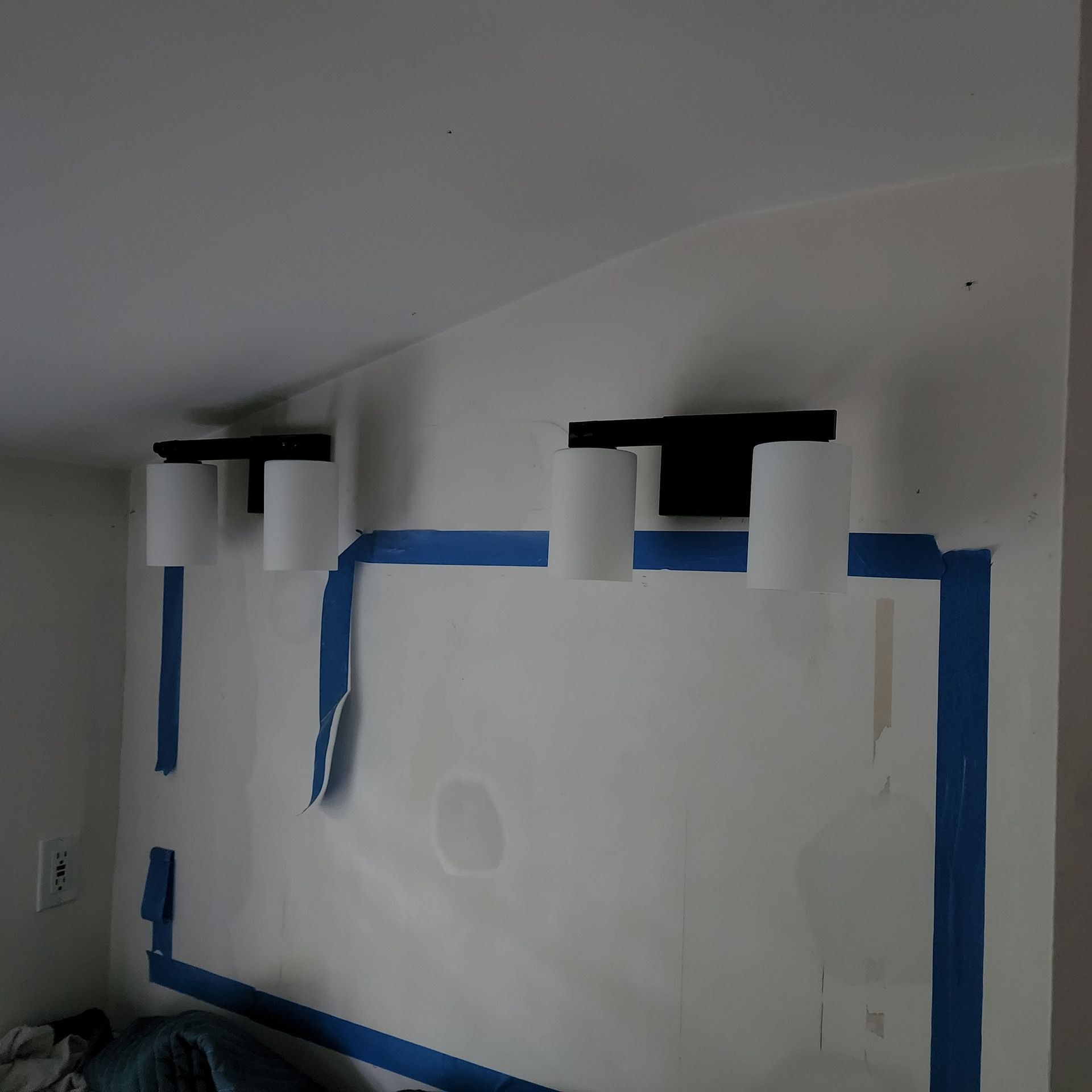 Blue painter’s tape outlining a wall-mounted rectangular area with two black bracketed fixtures above it