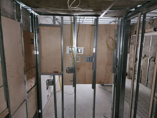Unfinished room framed with metal studs, exposed wiring, and plywood wall panels under construction.