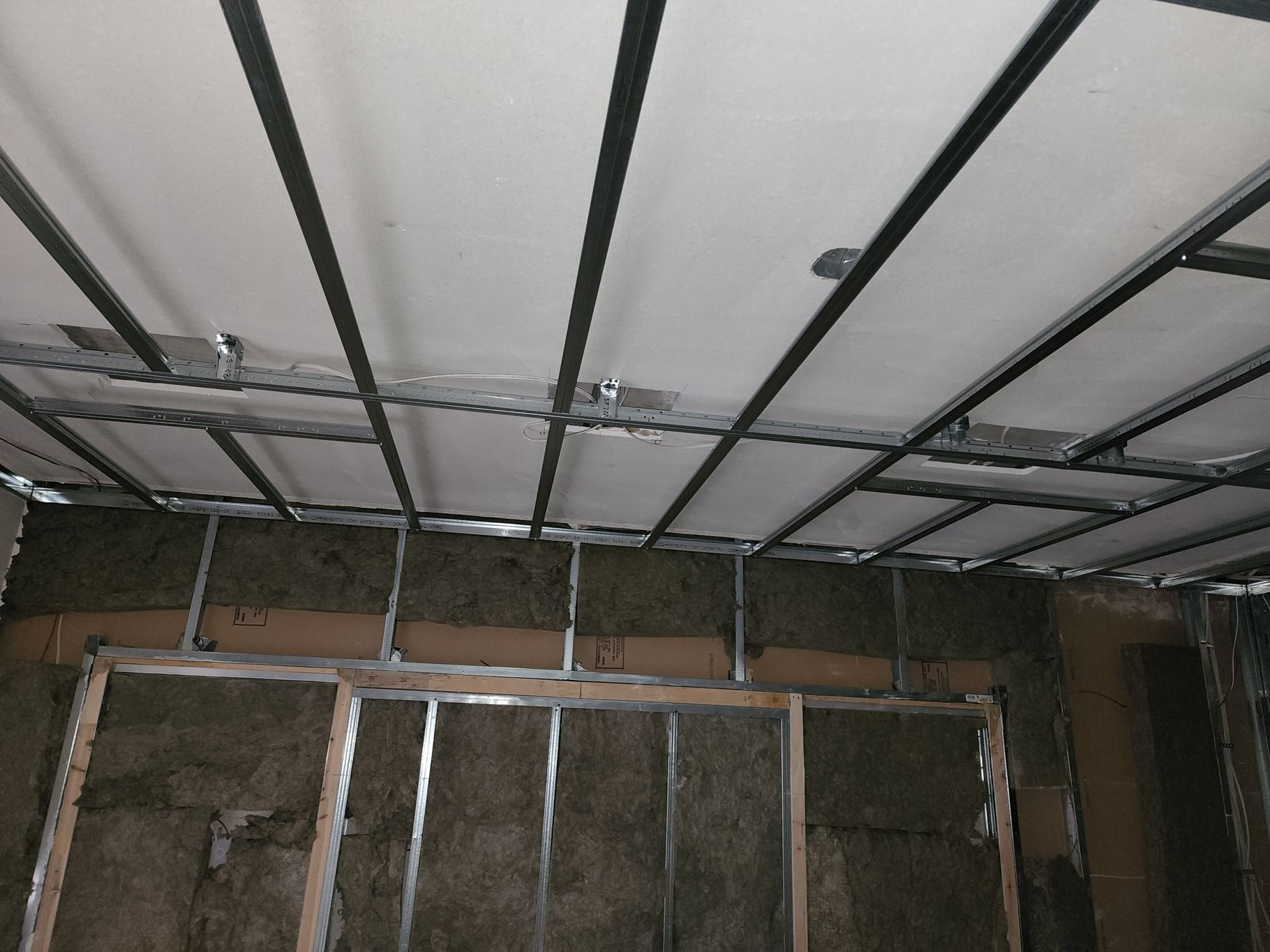 Interior wall under construction with exposed framing, insulation, and unfinished ceiling panels