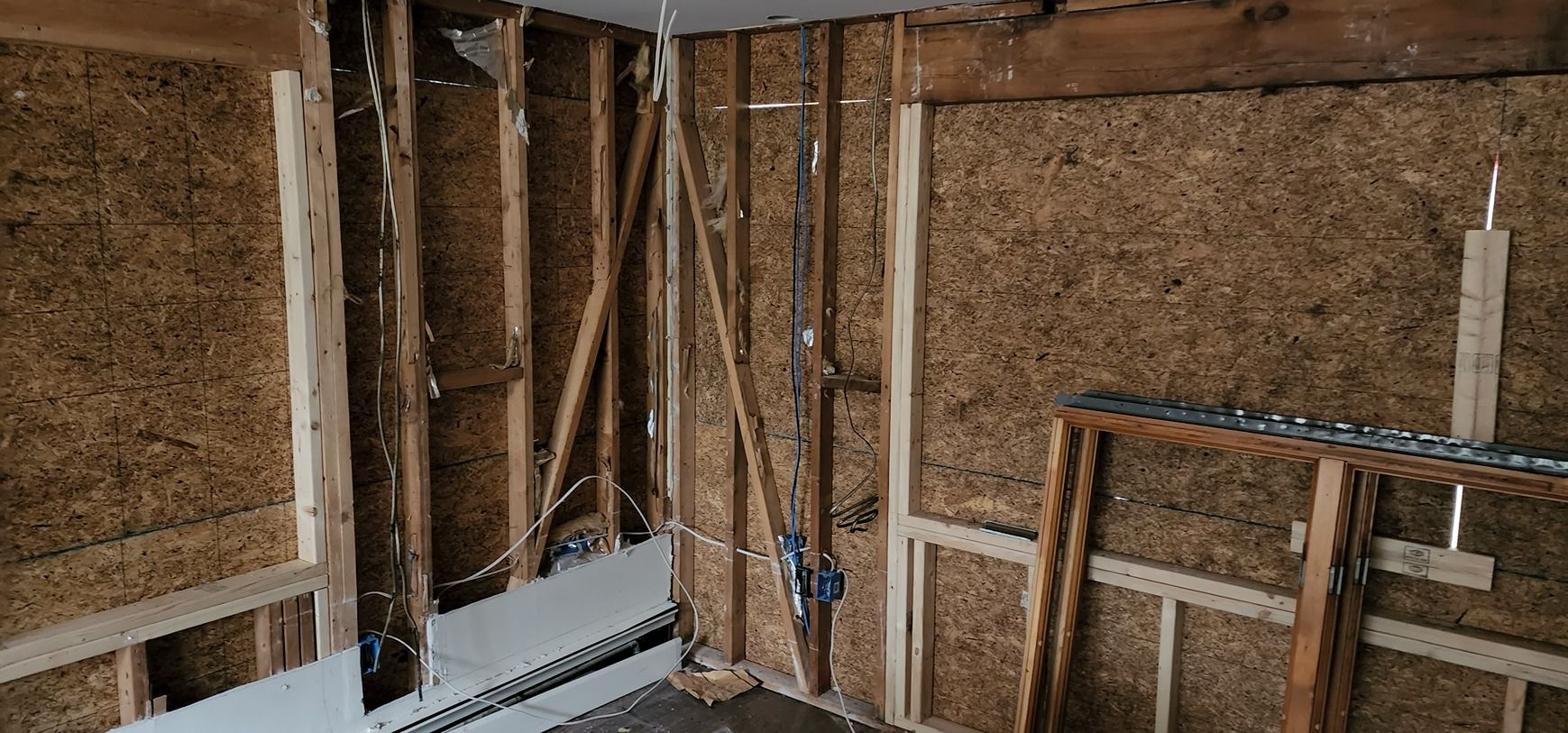 Partially stripped wall interior with exposed studs, insulation, and electrical wiring during renovation