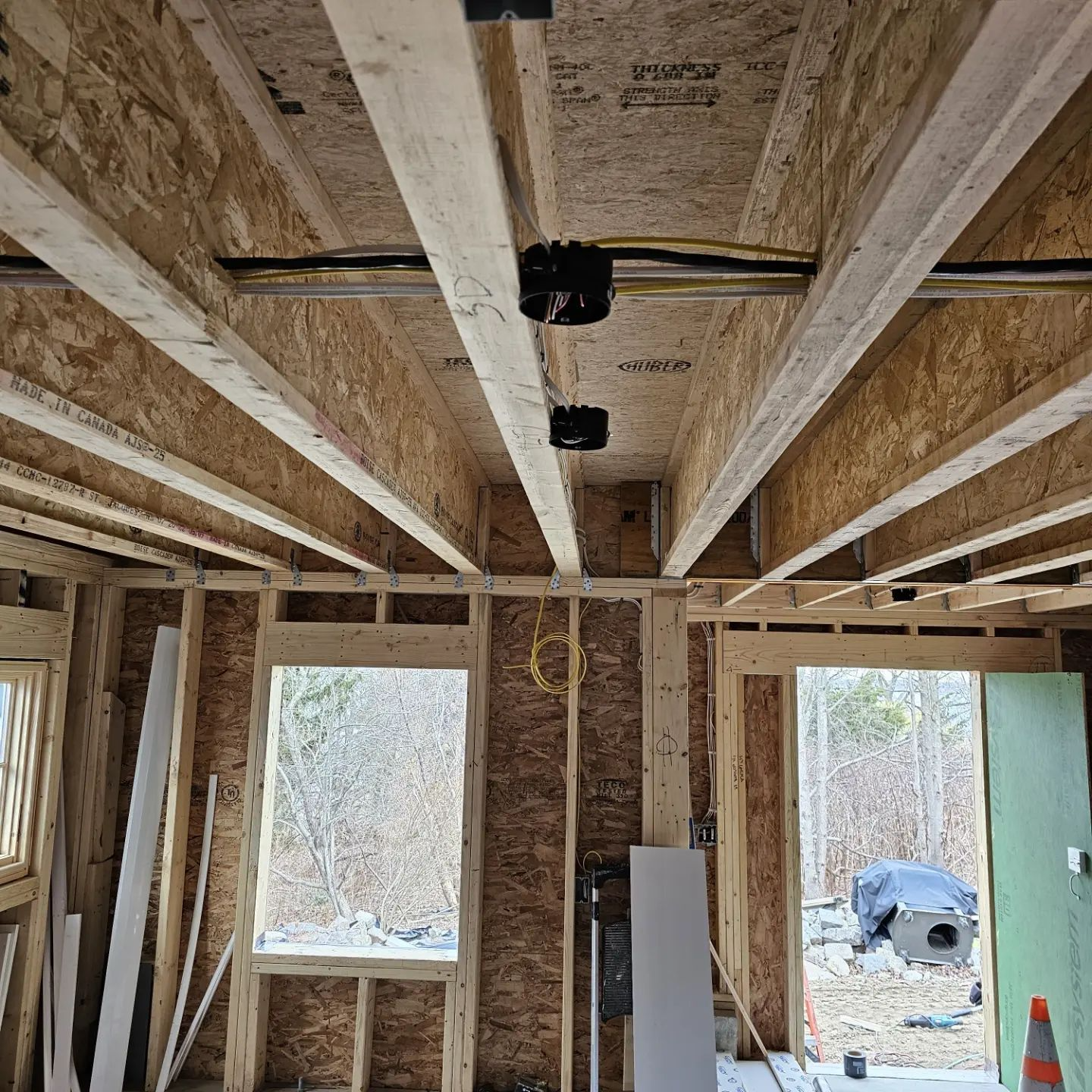 Interior of a house under construction, showing exposed wooden beams, framing, and open window and door openings.