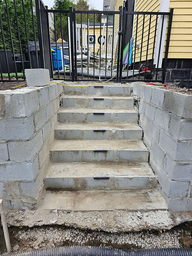Concrete steps leading up to a black metal gate, with cinder block retaining walls on both sides.