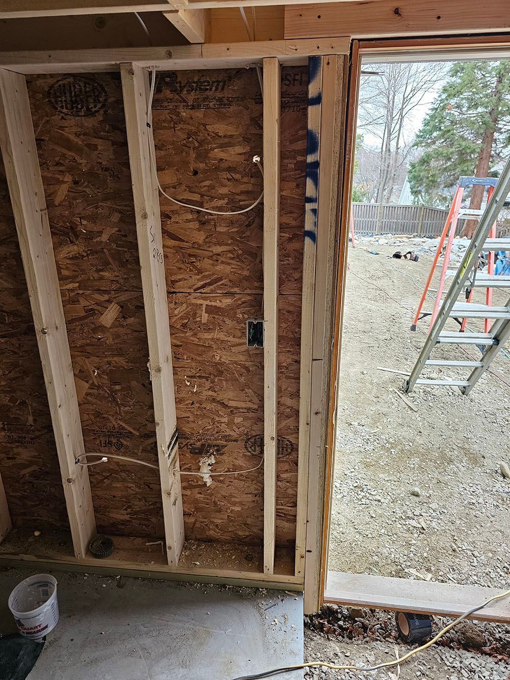 Interior wall framing with exposed insulation, open doorway, and ladder visible outside through the opening