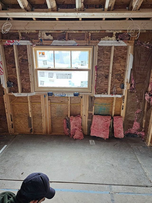 Interior wall under construction with exposed framing, a window, insulation, and a concrete floor.