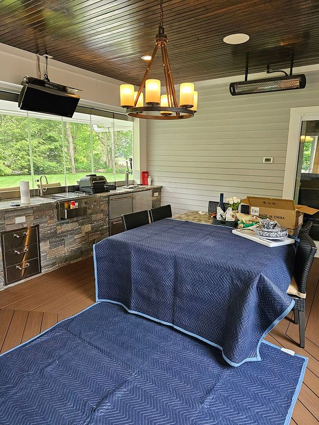 Covered patio dining area with blue tablecloth, chandelier, grill station, and outdoor seating.