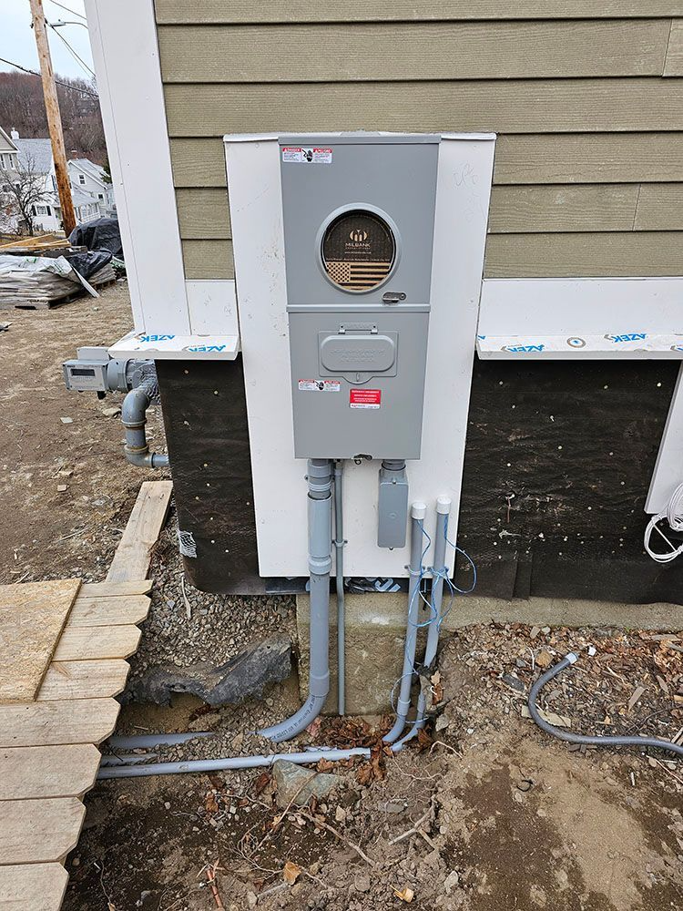 Gray electrical meter and service box mounted on a house exterior with conduit running into the ground.