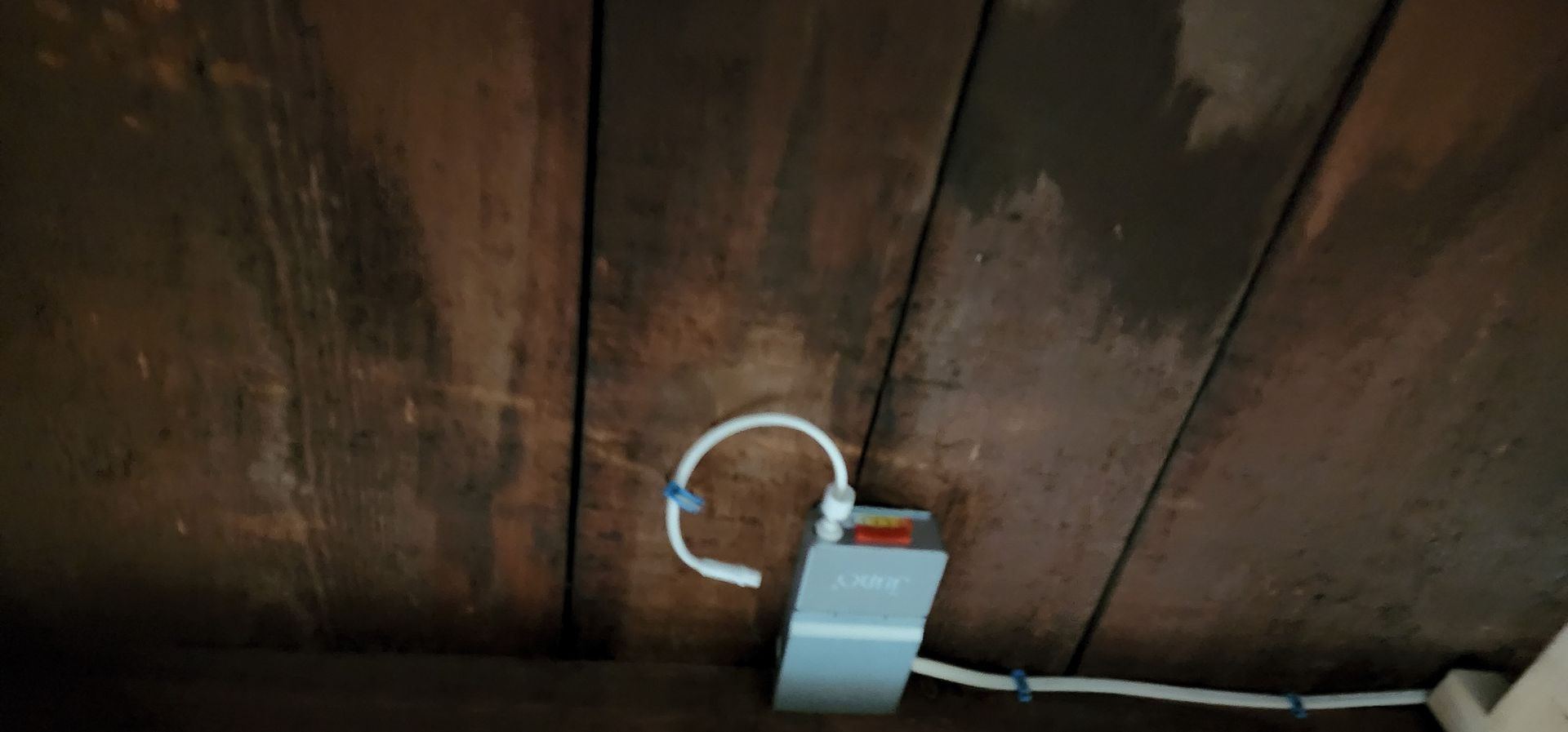 White USB charger plugged into an outlet beneath a wooden wall panel.