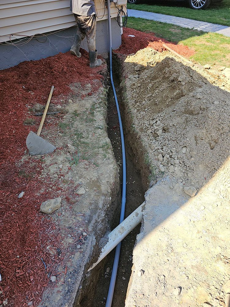 Trench beside a house with exposed blue conduit, dirt piles, shovel, and a utility pole base