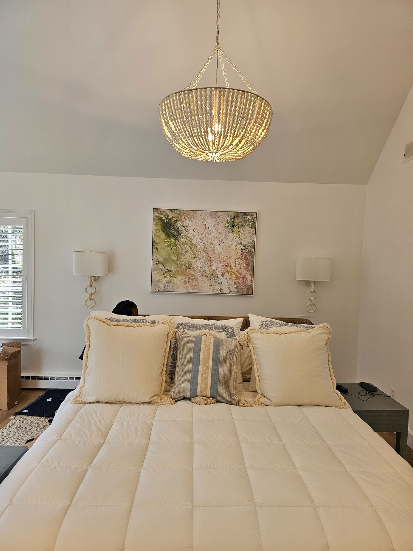 Bright bedroom with a chandelier, cream bedding, and floral wall art above the bed.