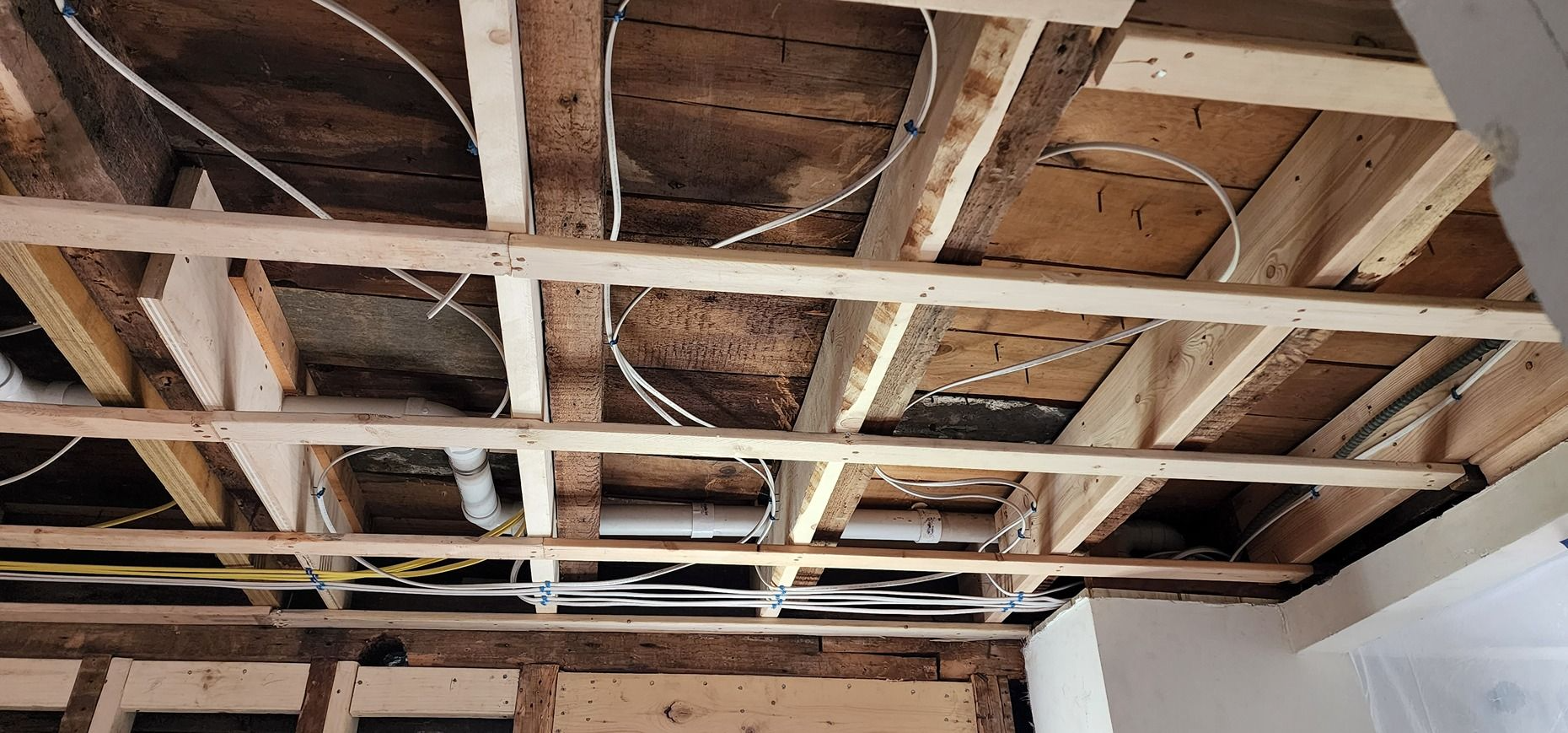 Exposed wooden ceiling joists with insulation and a white wall in a room under renovation