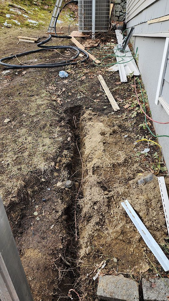 Narrow dirt walkway beside a house, with scattered white boards and a hose along the edge.