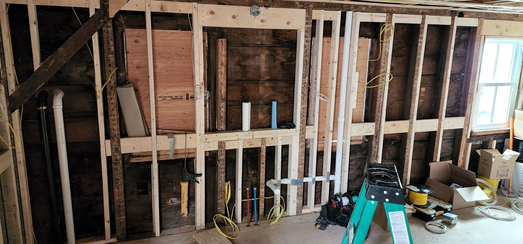 Partially framed interior wall under construction with exposed studs, insulation, and scattered tools on the floor