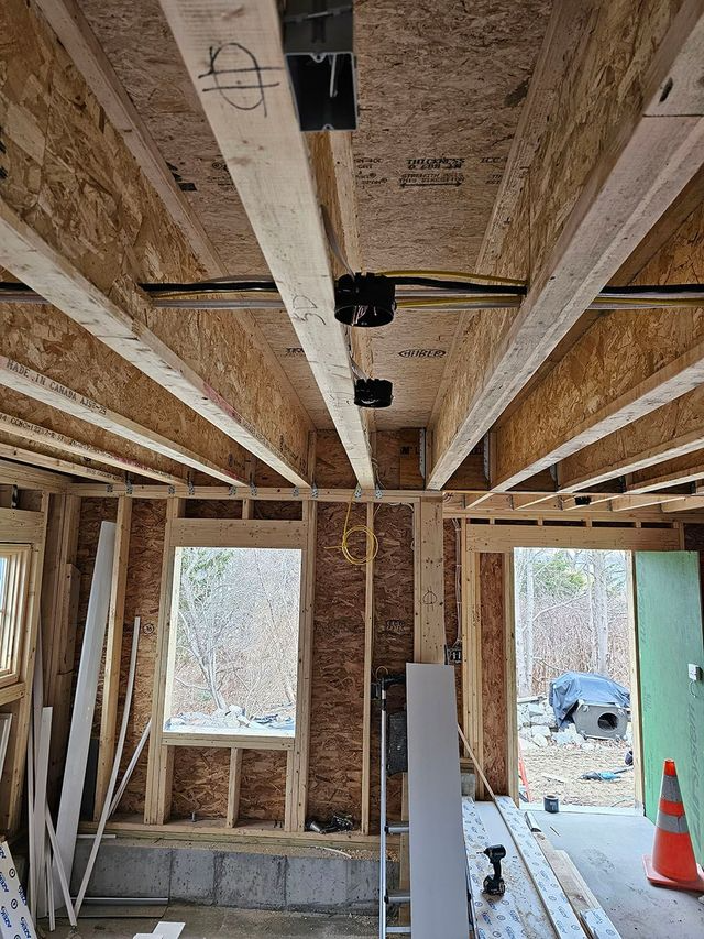 Interior of a house under construction with exposed ceiling joists, wall framing, and windows.
