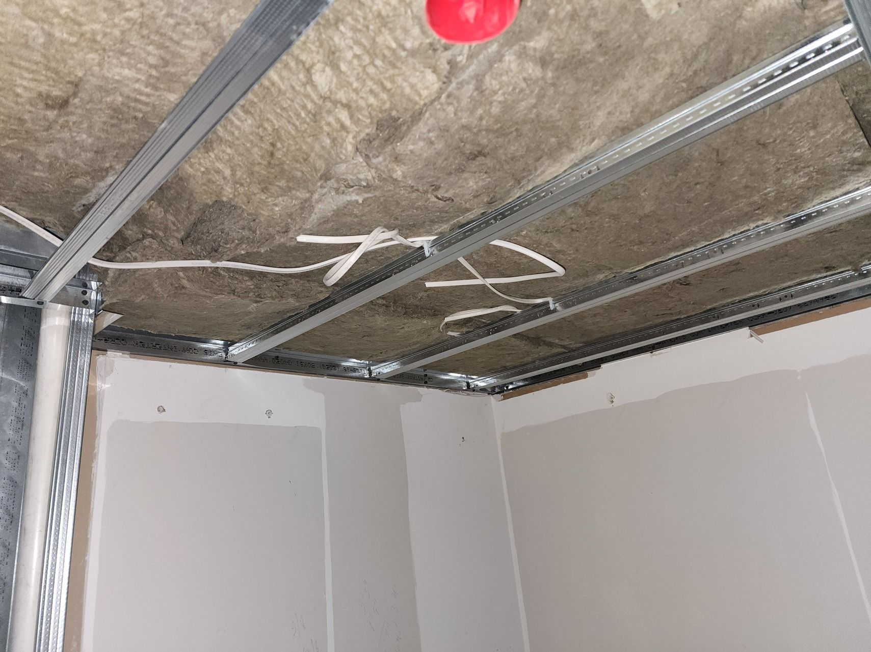 Unfinished room ceiling with metal framing, insulation, and a red light bulb hanging overhead