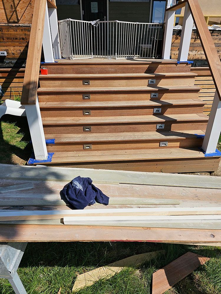 Wooden deck stairs under construction with white railings and lumber laid out in front