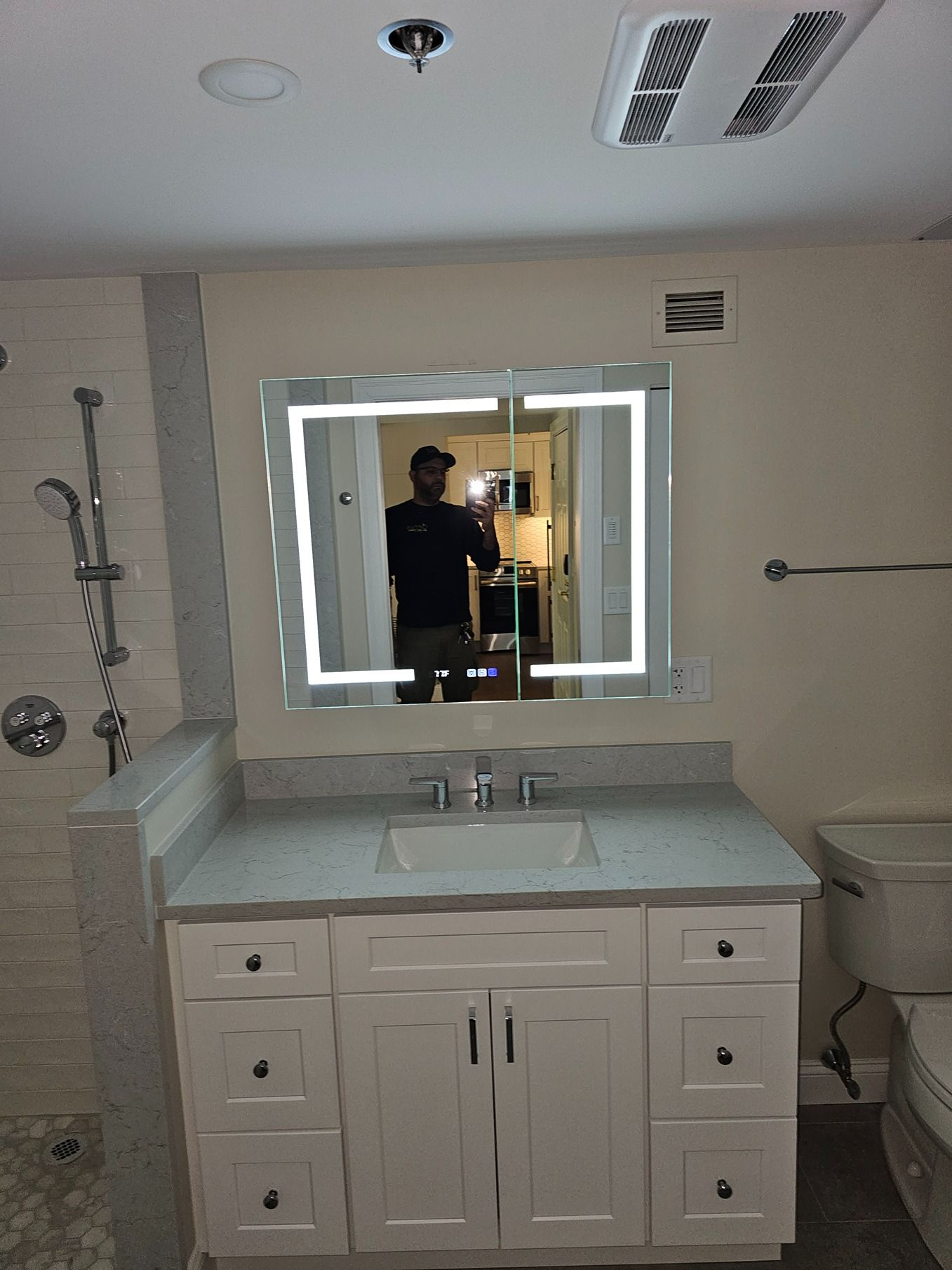 Bathroom vanity with lit mirror, white cabinets, sink, and shower visible on the left.