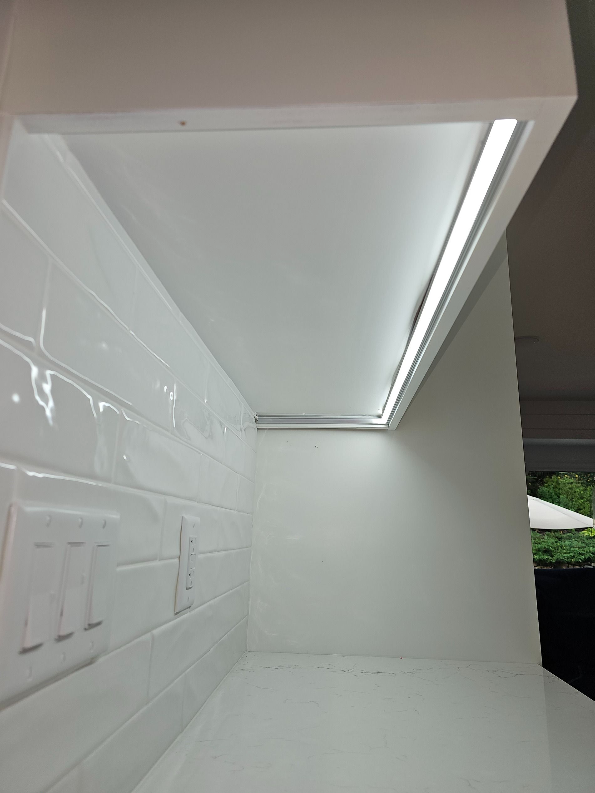 White tiled under-cabinet area with a long LED strip light and countertop storage space