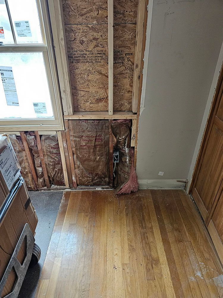 Partially demolished room with exposed wall studs, insulation, and hardwood floor near a window and closet edge