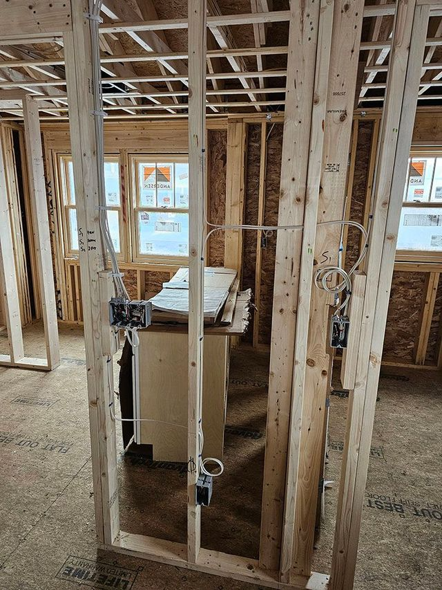Interior of unfinished house with exposed framing, wiring, and a small cabinet in the center