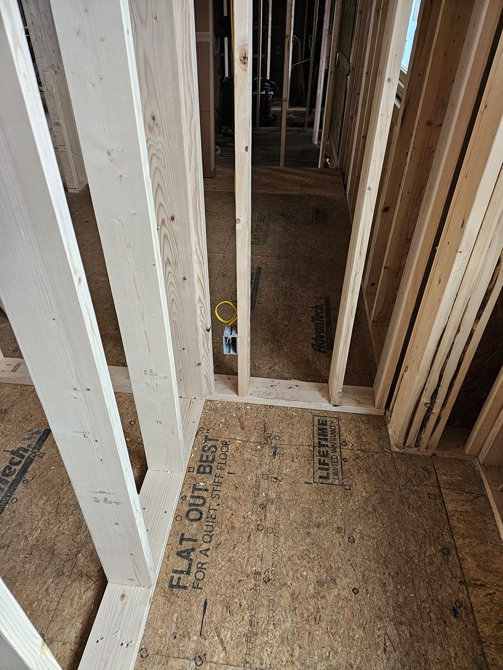 Framed wall studs and plywood flooring in an unfinished construction area.