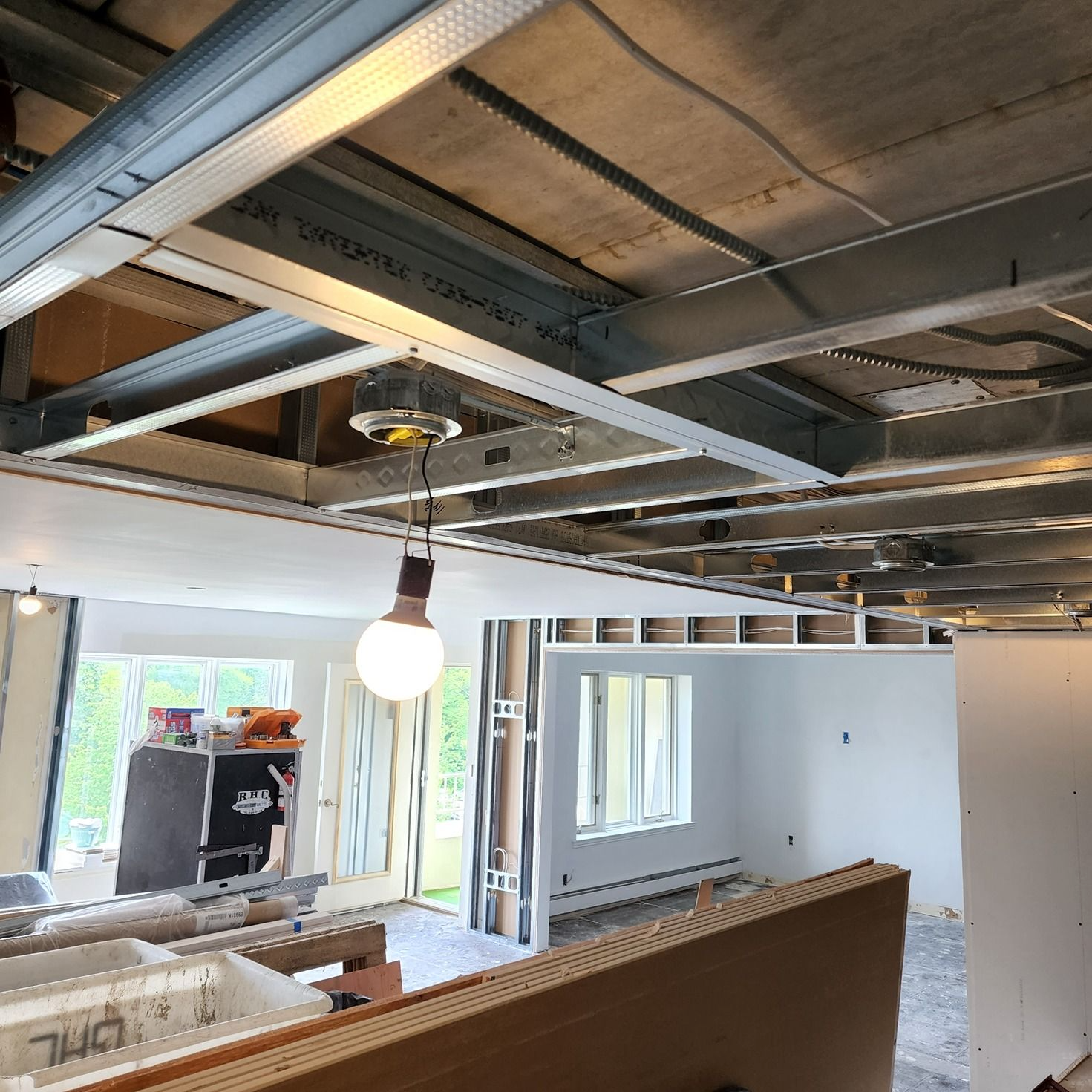 Interior under construction with exposed ceiling beams, hanging light bulb, and unfinished walls.