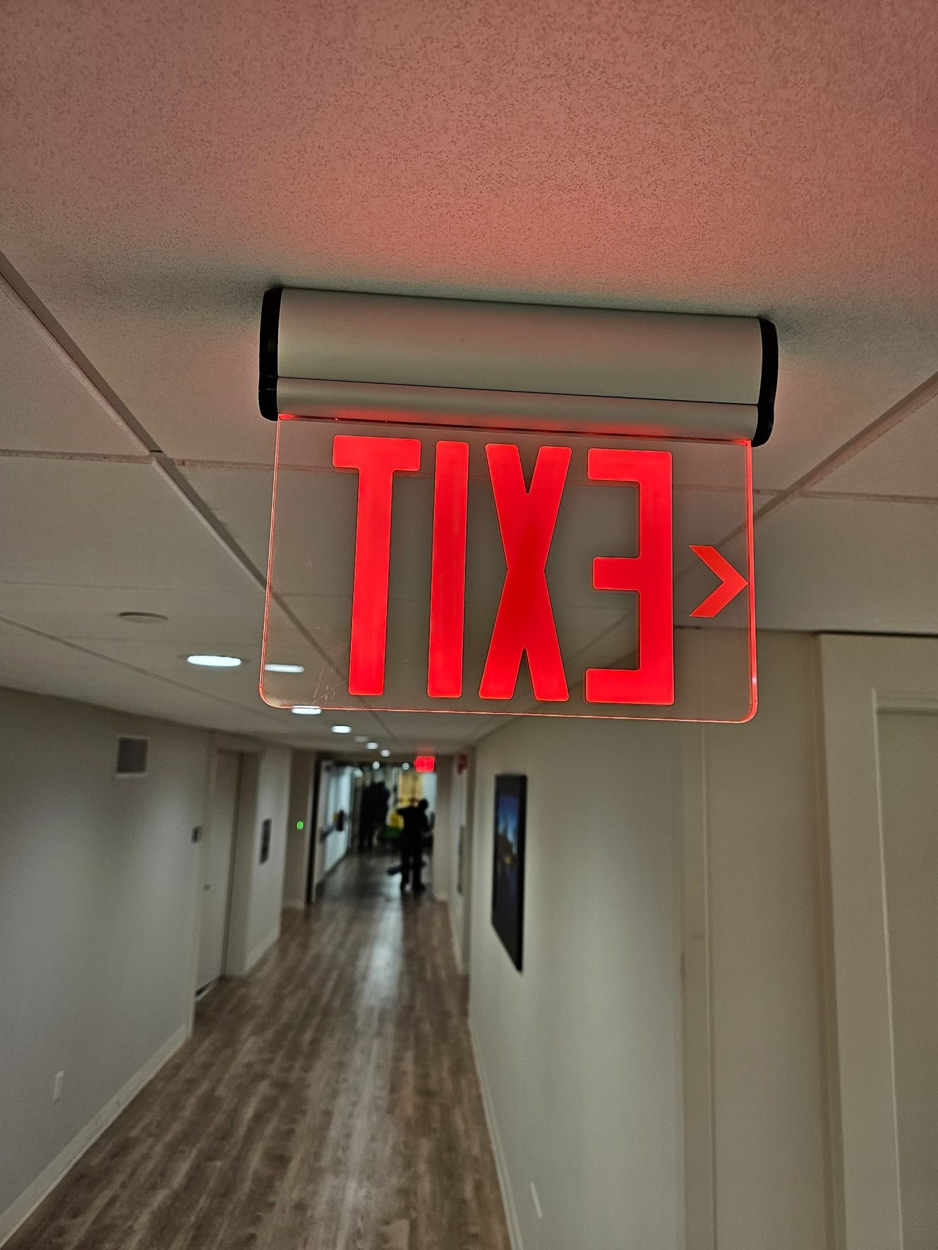 Hallway with a glowing red EXIT sign hanging from the ceiling, viewed upside down.