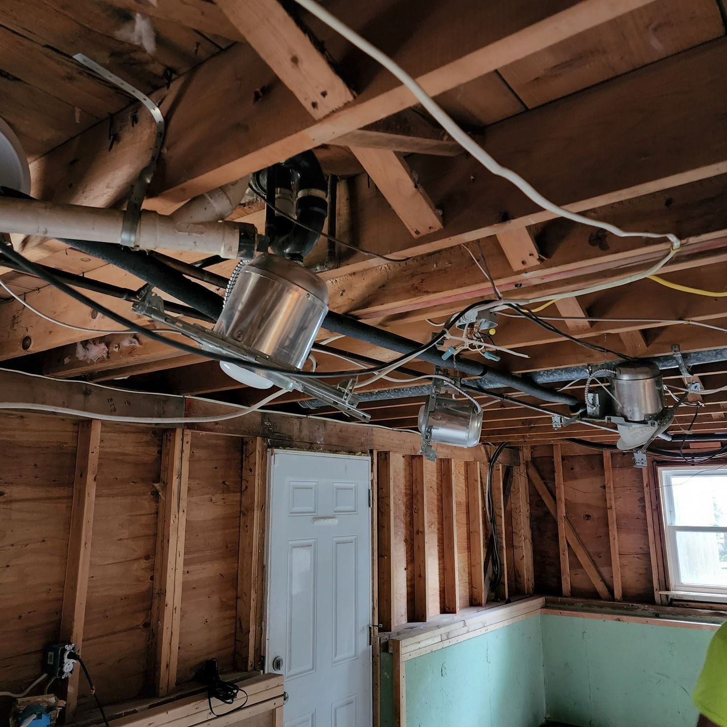 Exposed attic framing with ductwork, wiring, a white door, and a green wall under construction