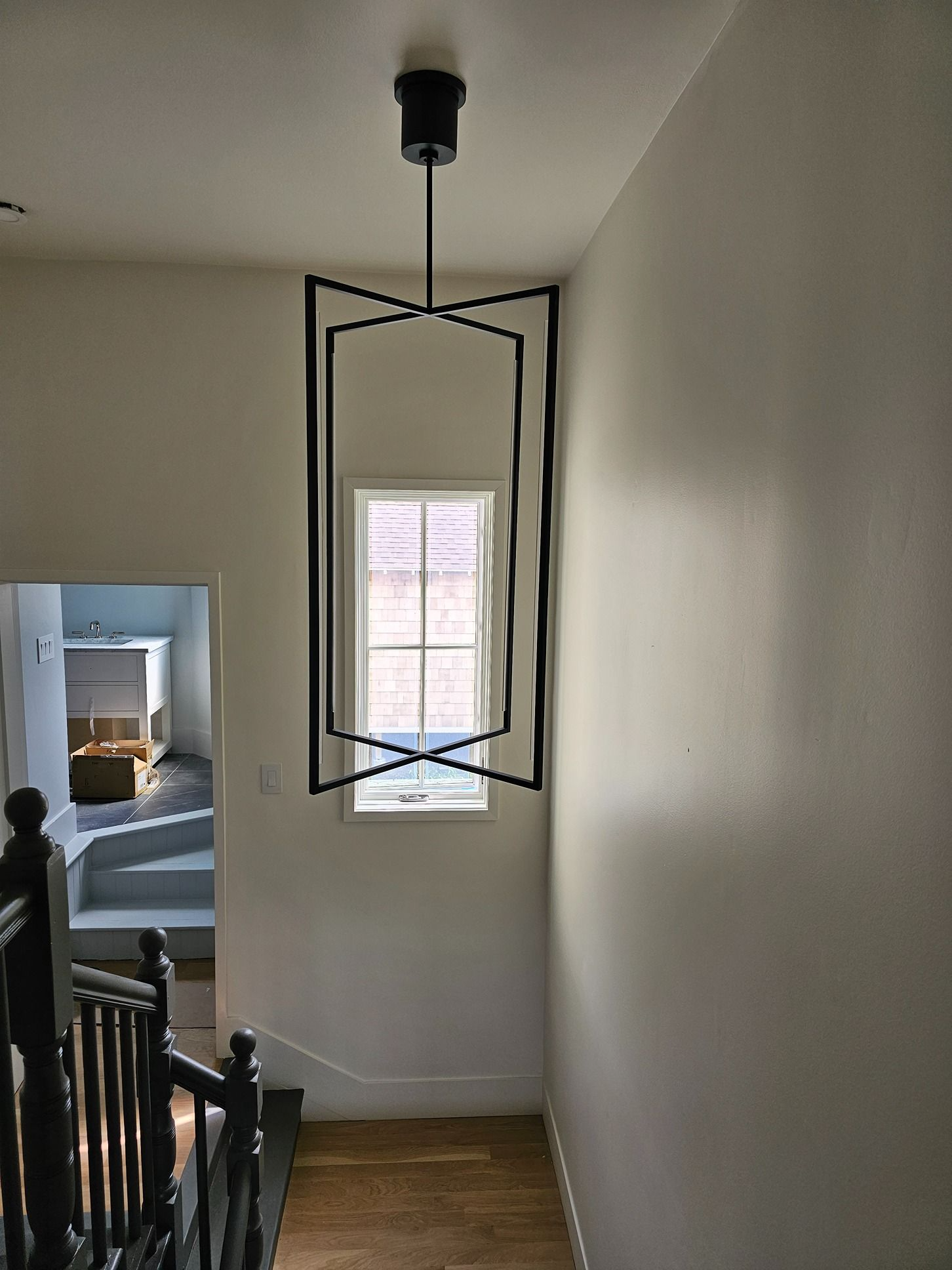 Stair landing with black pendant light hanging before a small window and railing below.
