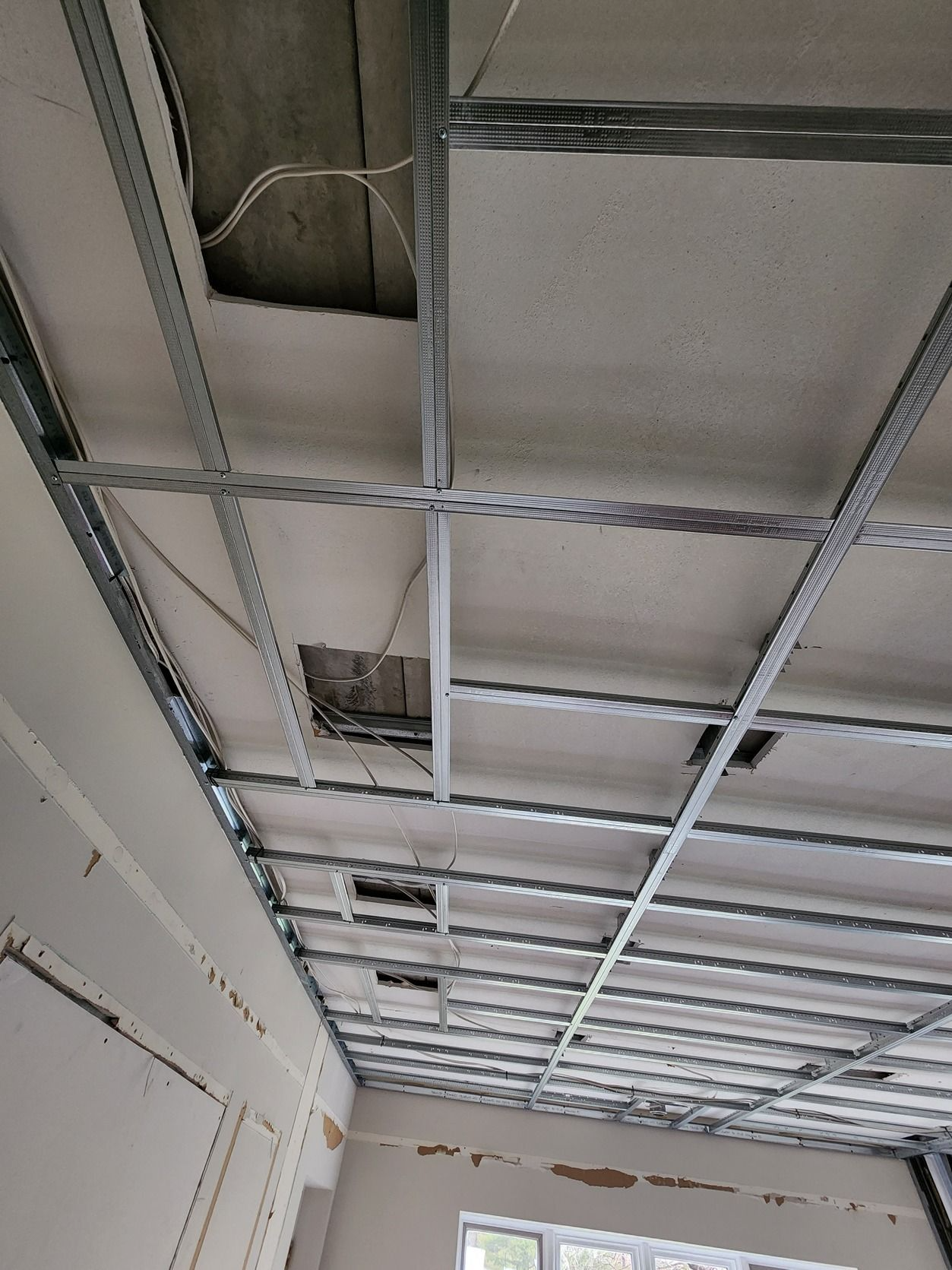Exposed ceiling grid with missing panels and visible wiring in an unfinished interior room