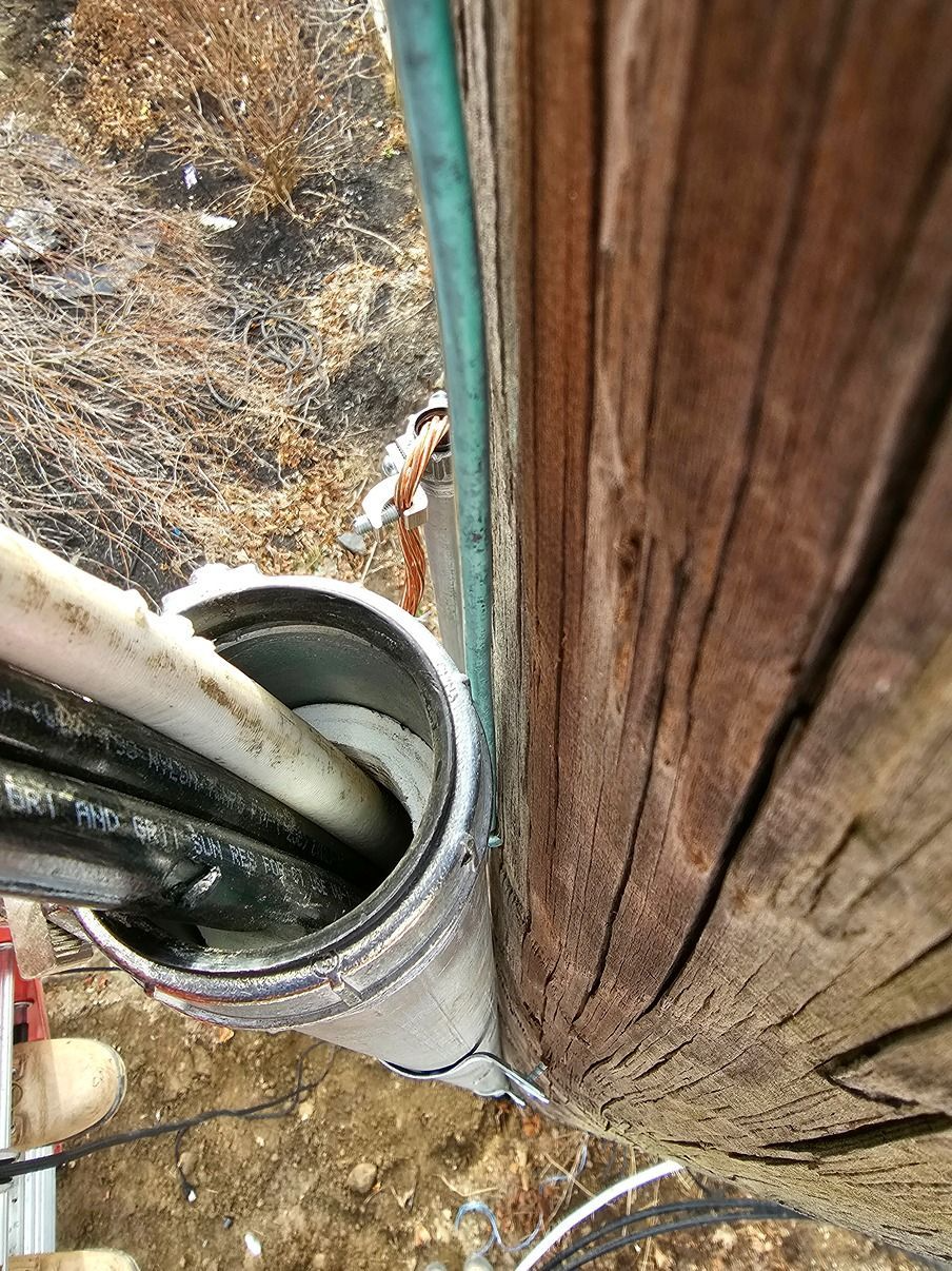 Close-up of cables entering a metal conduit beside weathered wooden siding outdoors