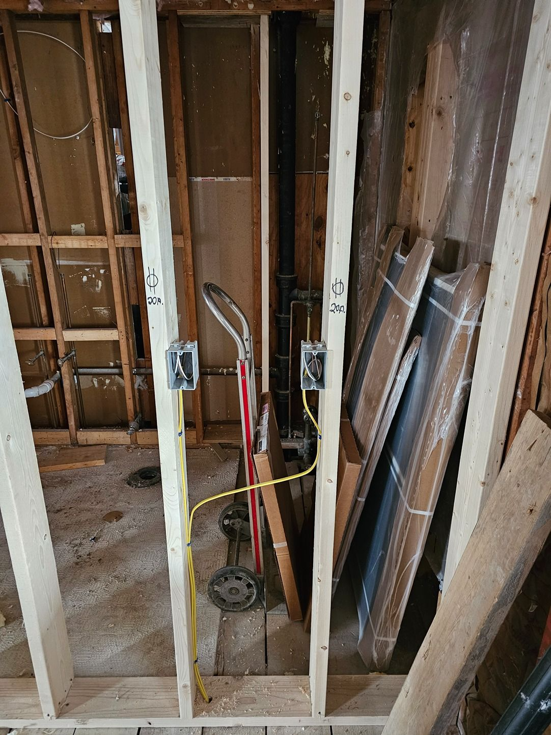 Open wall framing with exposed plumbing, wiring, and tools in a partially renovated room.