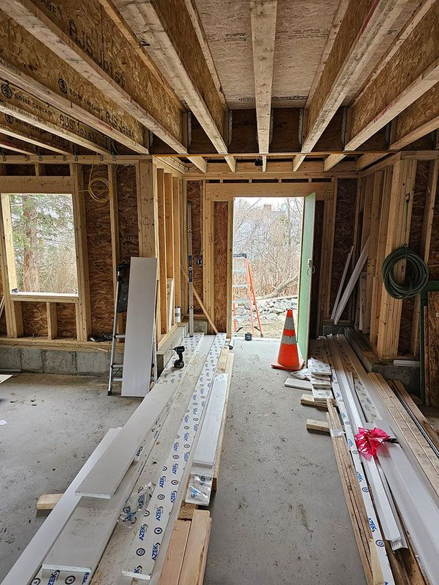 Interior of a house under construction with exposed wooden beams, insulation, and building materials scattered on the floor.