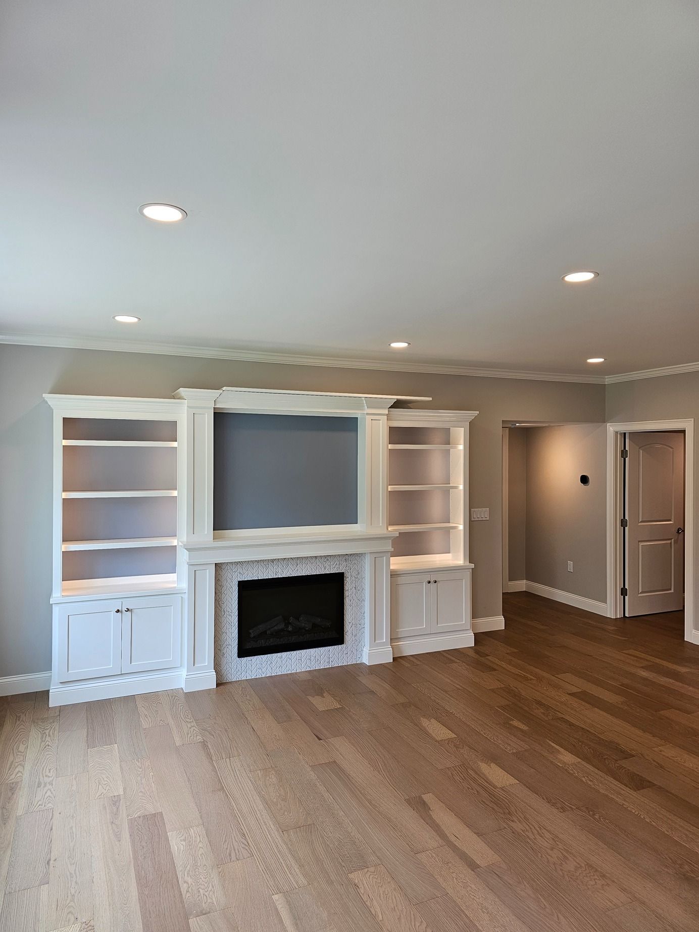 Empty living room with built-in white shelves, fireplace, hardwood floors, and recessed ceiling lights