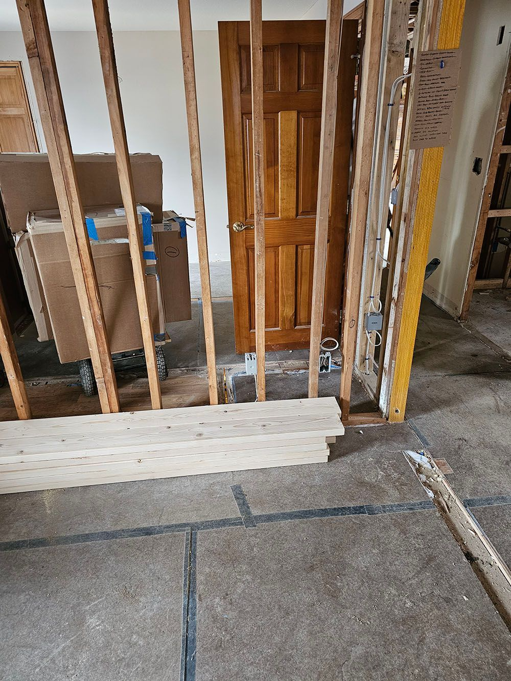 Indoor construction site with exposed studs, drywall, and a wooden doorframe near a concrete floor.