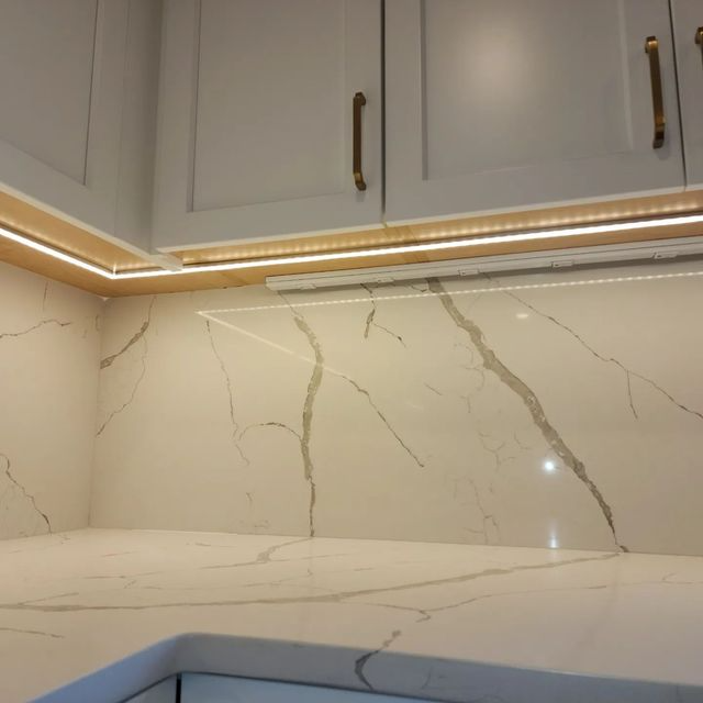 Modern kitchen backsplash with white marble-look countertop, gray cabinets, and warm under-cabinet lighting