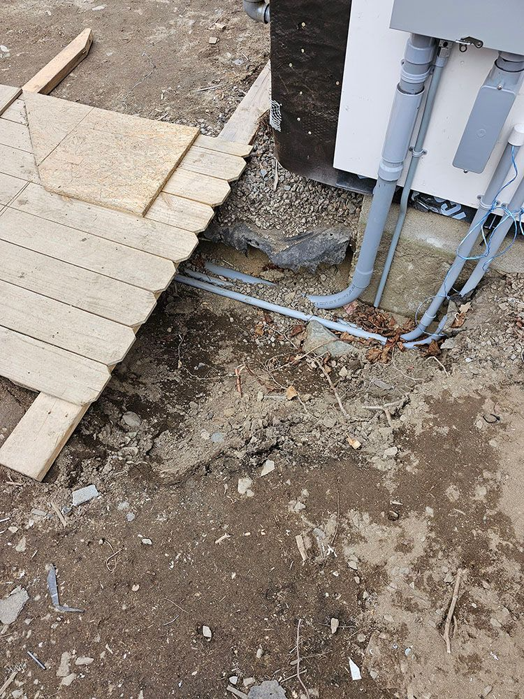 Outdoor utility pipes beside a paved walkway, with exposed dirt and construction debris nearby