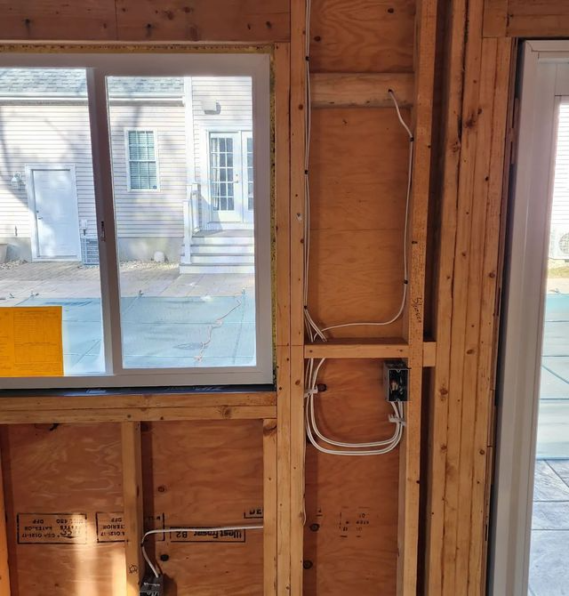 Unfinished wooden wall framing with a window and exposed electrical wiring inside a building under construction