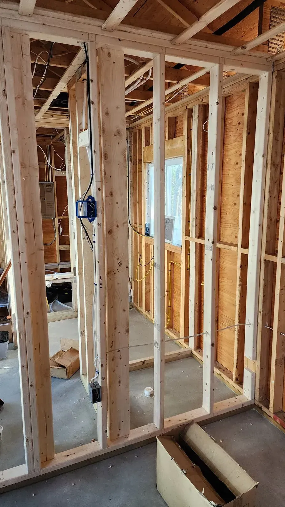 Framed interior wall under construction with exposed studs, wiring, and a blue electrical box.