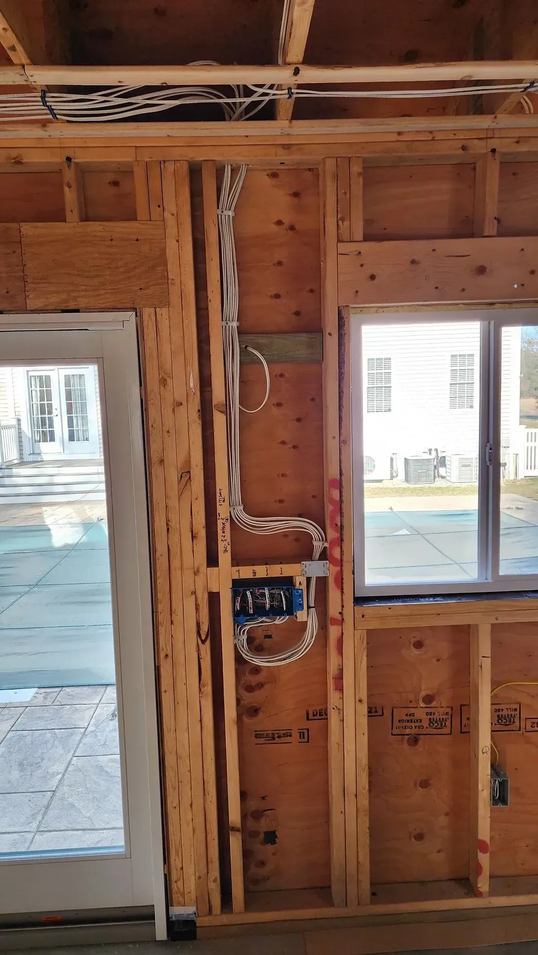 Unfinished wood wall framing with wiring and two windows, viewed from inside a construction site