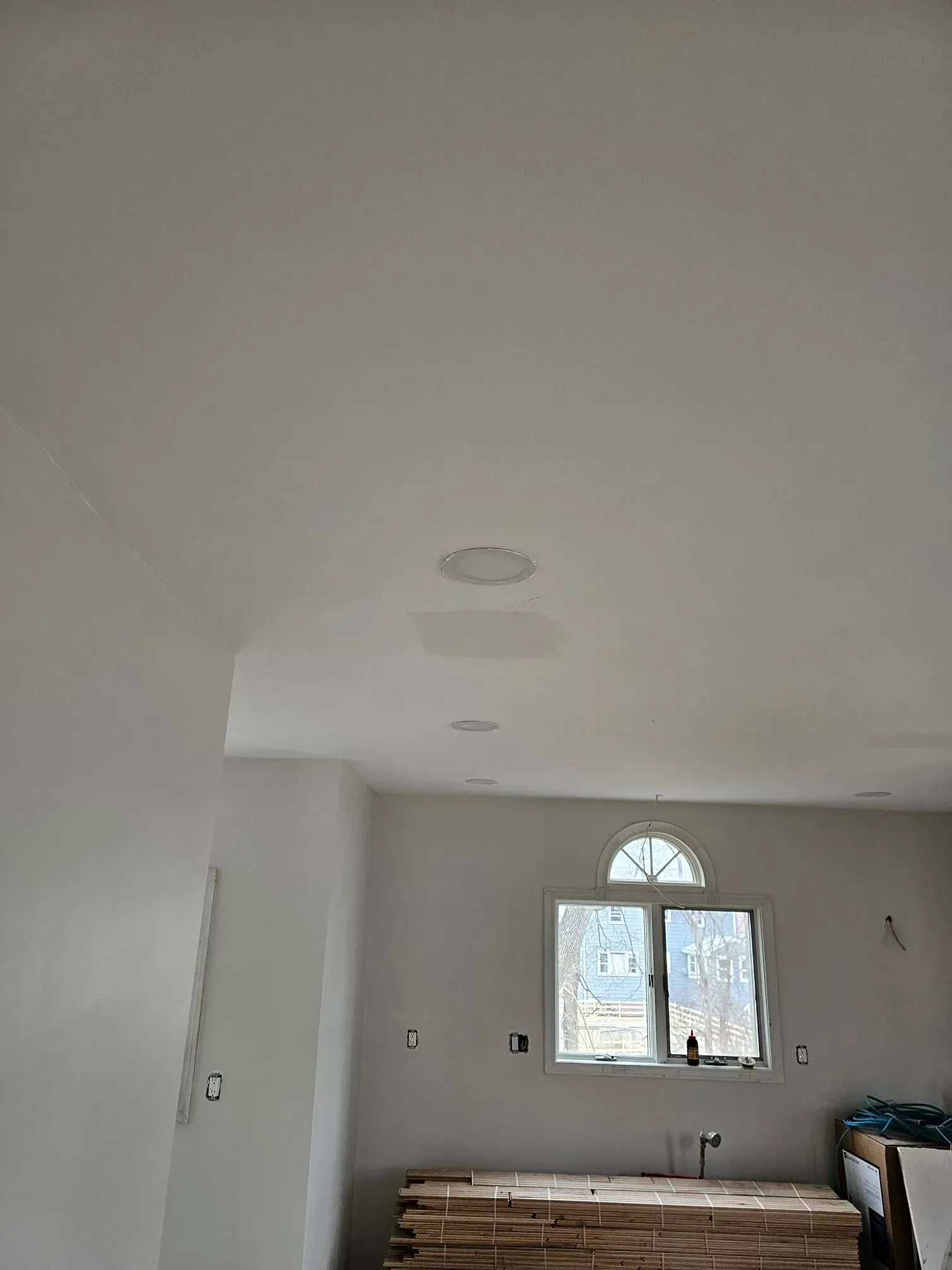 Bright, unfinished room with white walls, a window, and a partially visible bed or furniture.