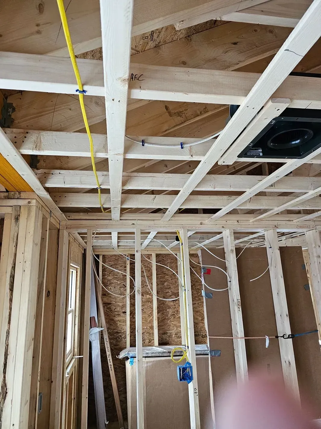 Framed interior under construction with exposed ceiling joists, wiring, and a hanging light cord.