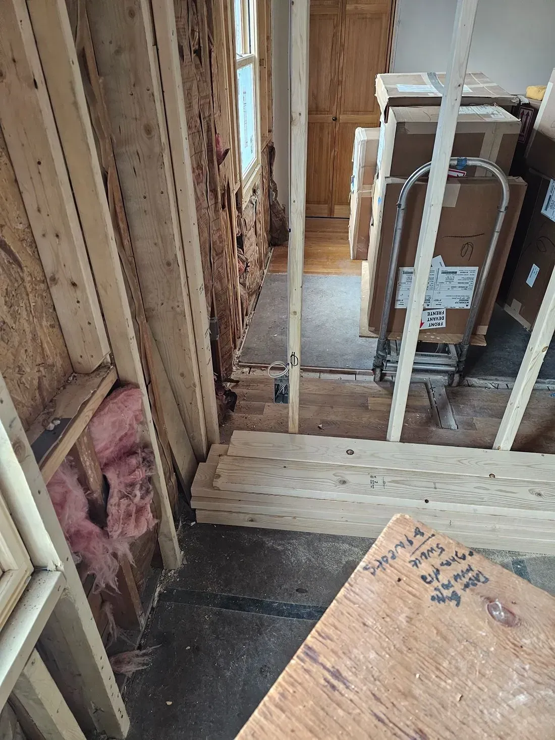 Partially gutted interior wall framing with exposed studs, insulation, and construction materials on the floor