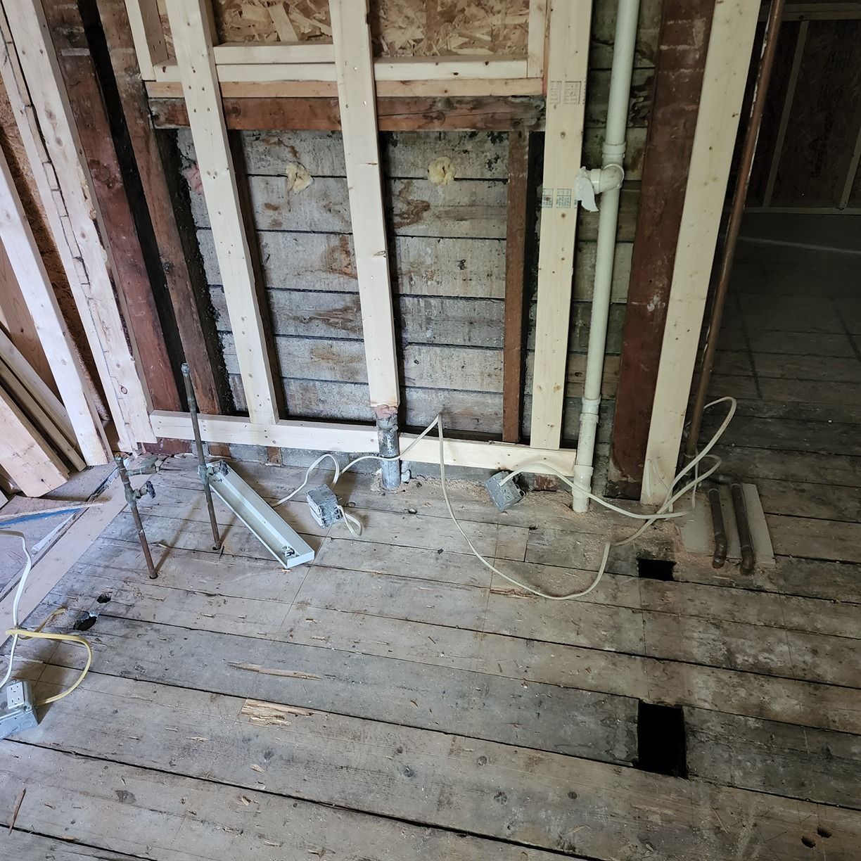 Exposed wall studs and old wooden floor in a partially demolished room with debris scattered.