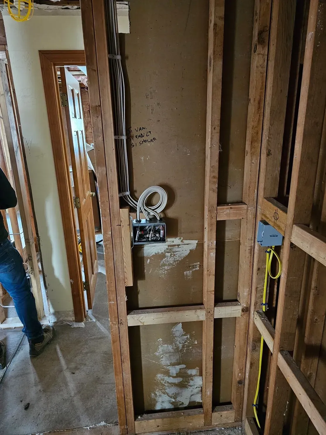 Partially framed interior wall with exposed wiring and plumbing in an unfinished hallway