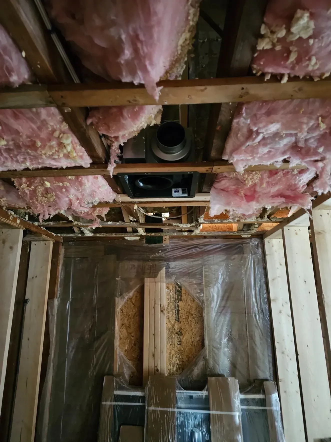 Unfinished room interior with exposed pink insulation, ceiling joists, and plastic-covered walls