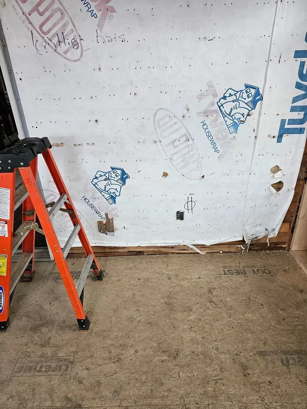Interior wall with scuffs and blue paint marks, a red ladder on the left, and a concrete floor.