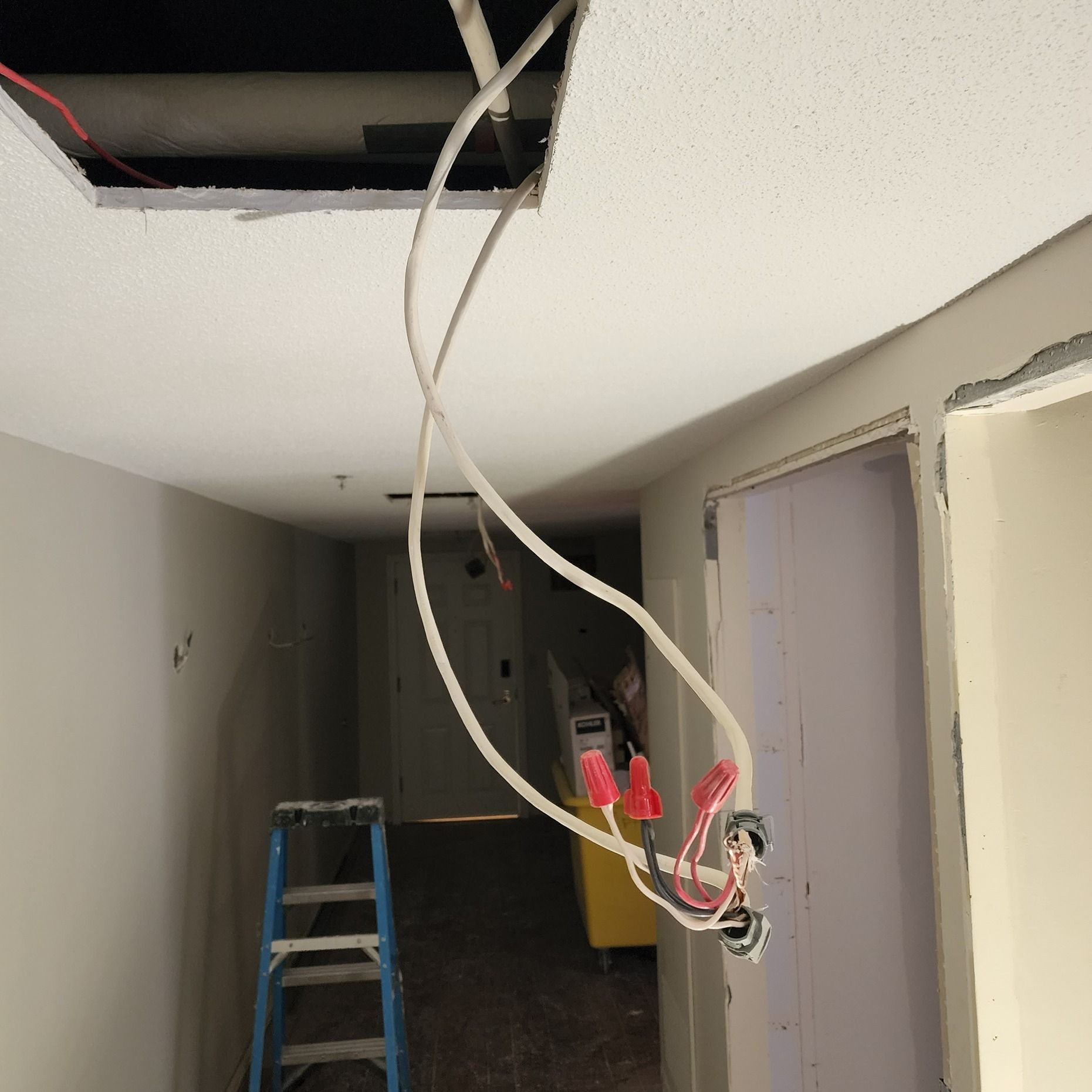 Partially finished hallway with exposed wiring, open ceiling panel, ladder, and tools on the floor