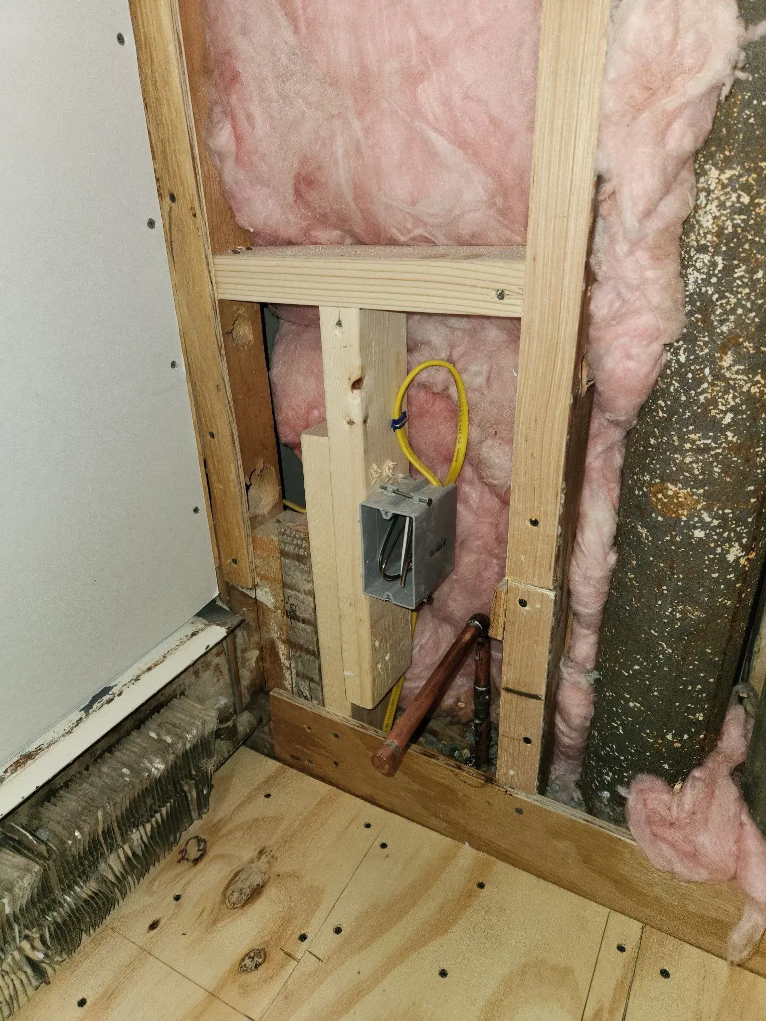 Open wall with pink insulation, exposed wiring, and a yellow-circled outlet box near the floor.